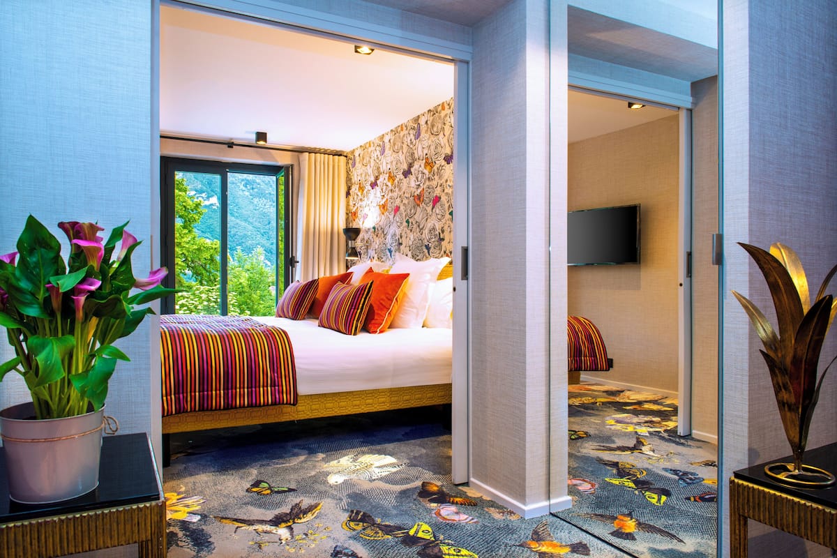 Habitación de hotel con cama, una planta en maceta, televisor y alfombra estampada.