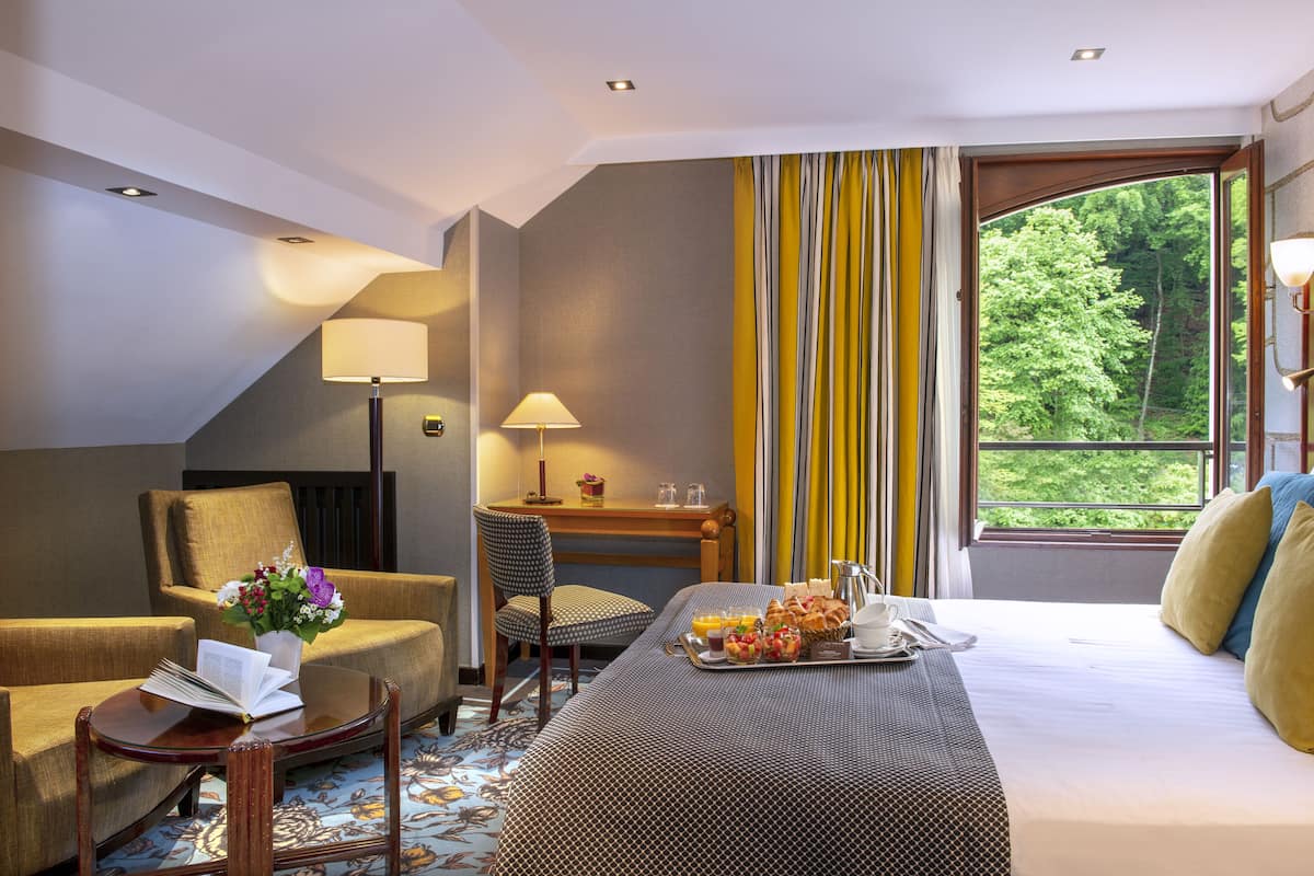 Habitación de hotel con cama, mesa de desayuno, una silla, escritorio y vista a zonas verdes.