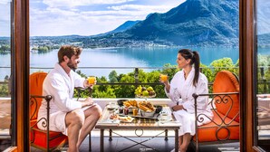 Un balcon avec une table préparée pour le petit-déjeuner, offrant une vue sur un lac et des montagnes.