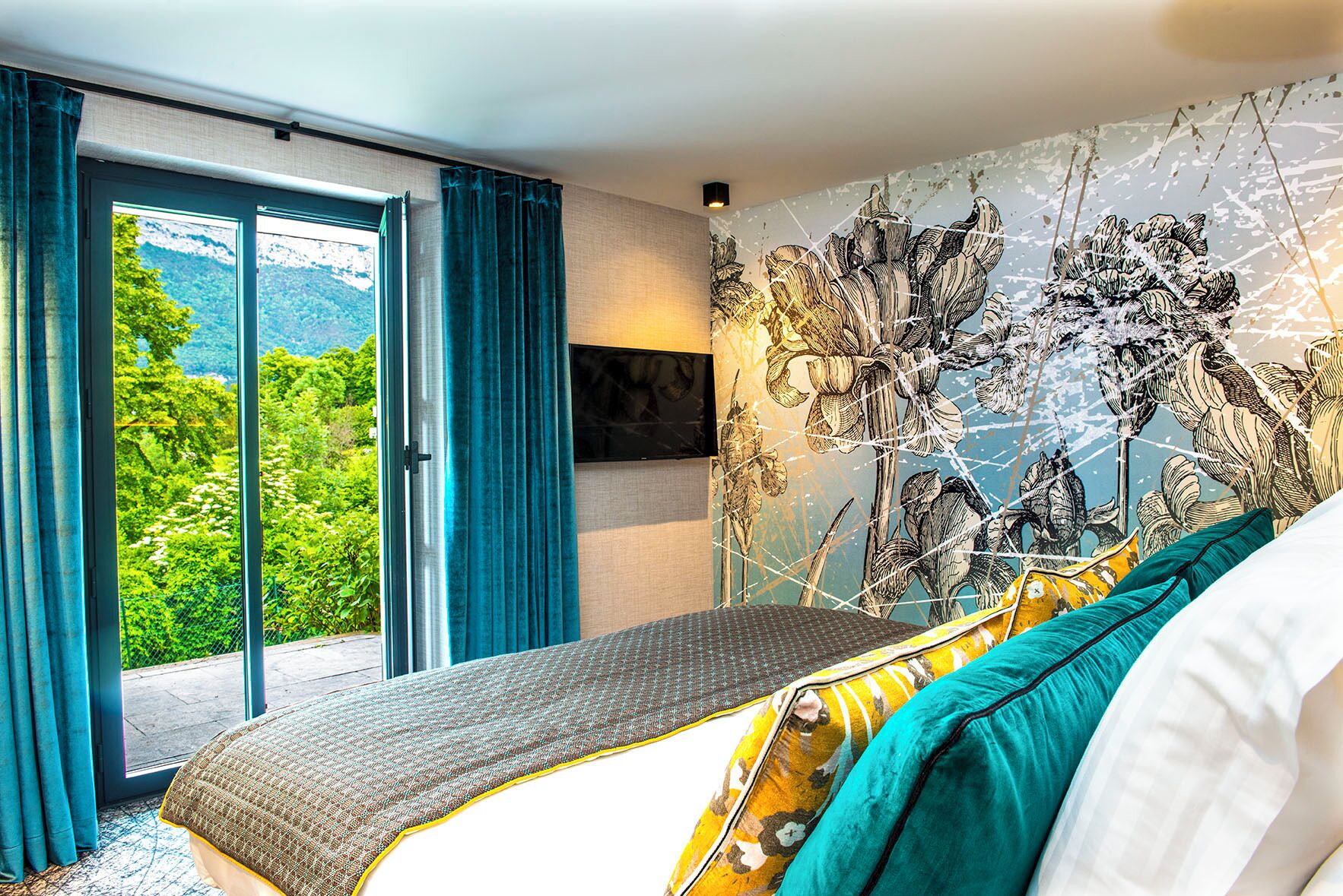 A bedroom with a bed, a large window, and a mural of flowers.
