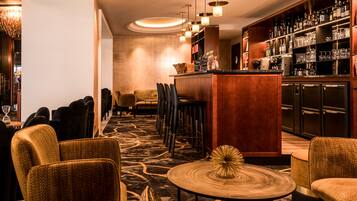 A bar area with a bar counter, stools, and a variety of bottles and glasses on shelves.
