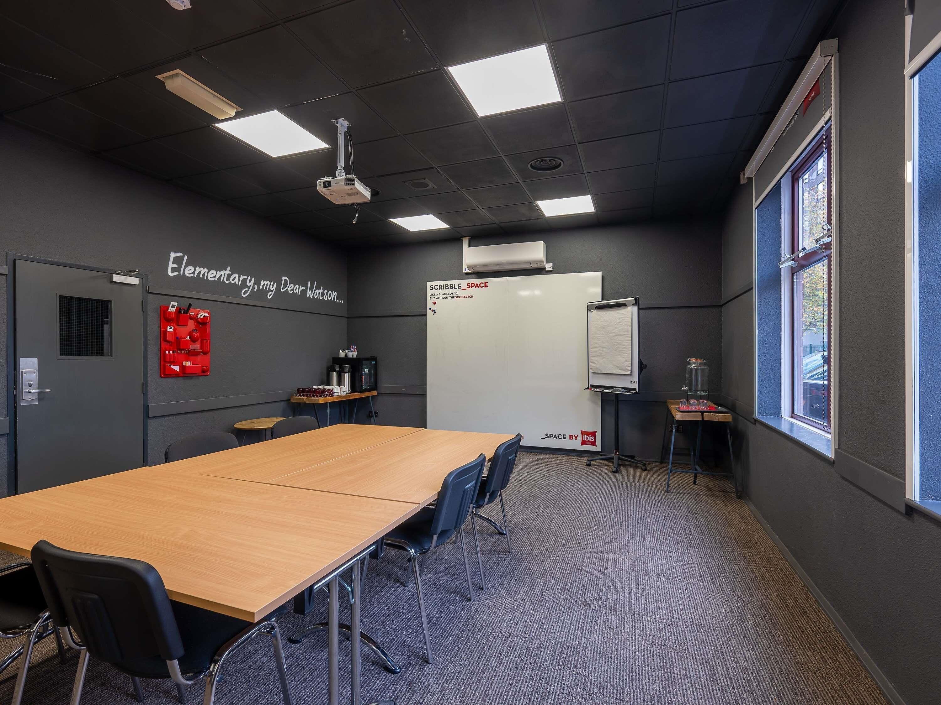 A conference room with a long table, chairs, a whiteboard, a projector, and a window.