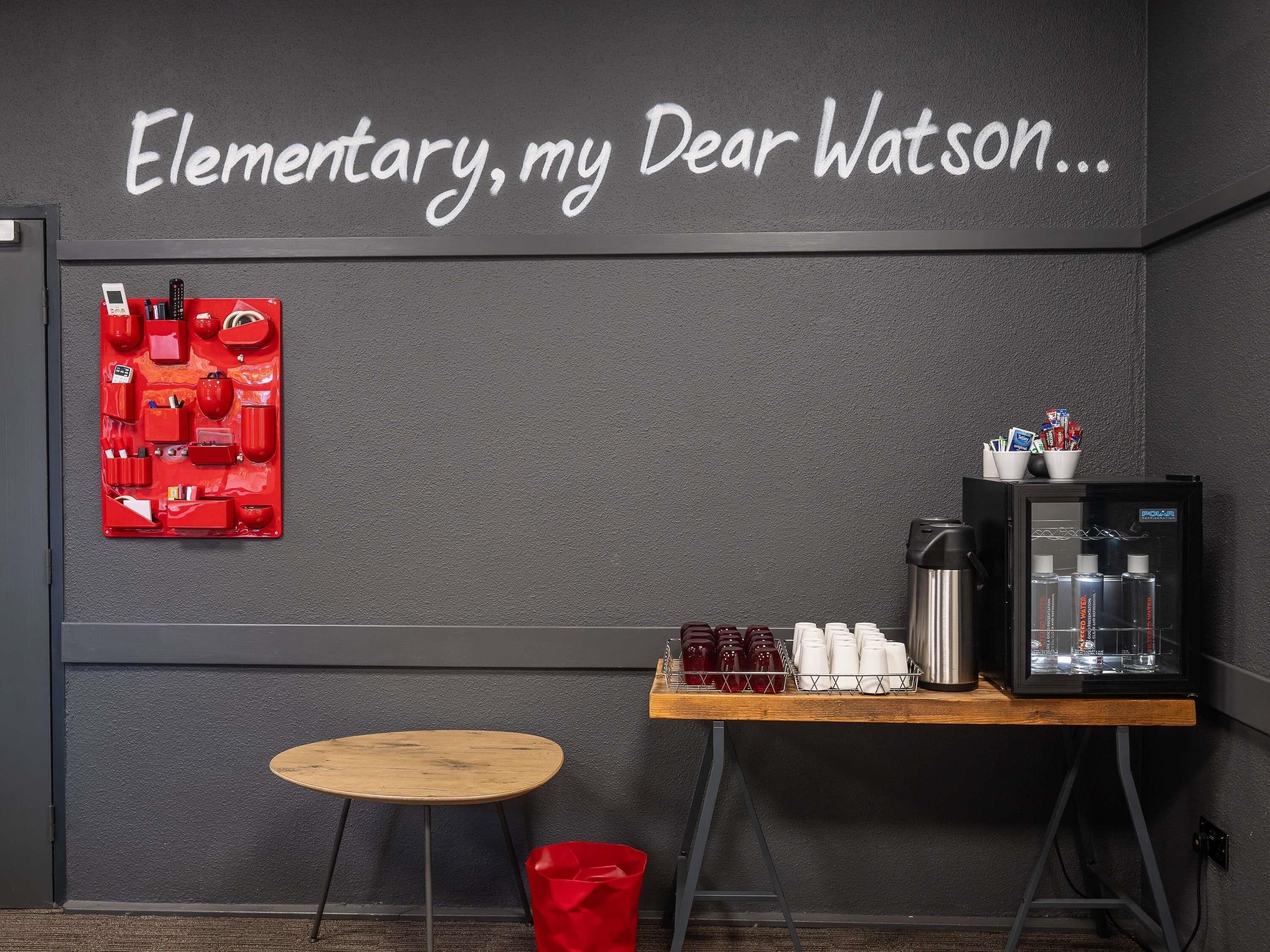 Una habitación con un panel de almacenamiento rojo instalado en la pared, una máquina de café y una pequeña mesa redonda.