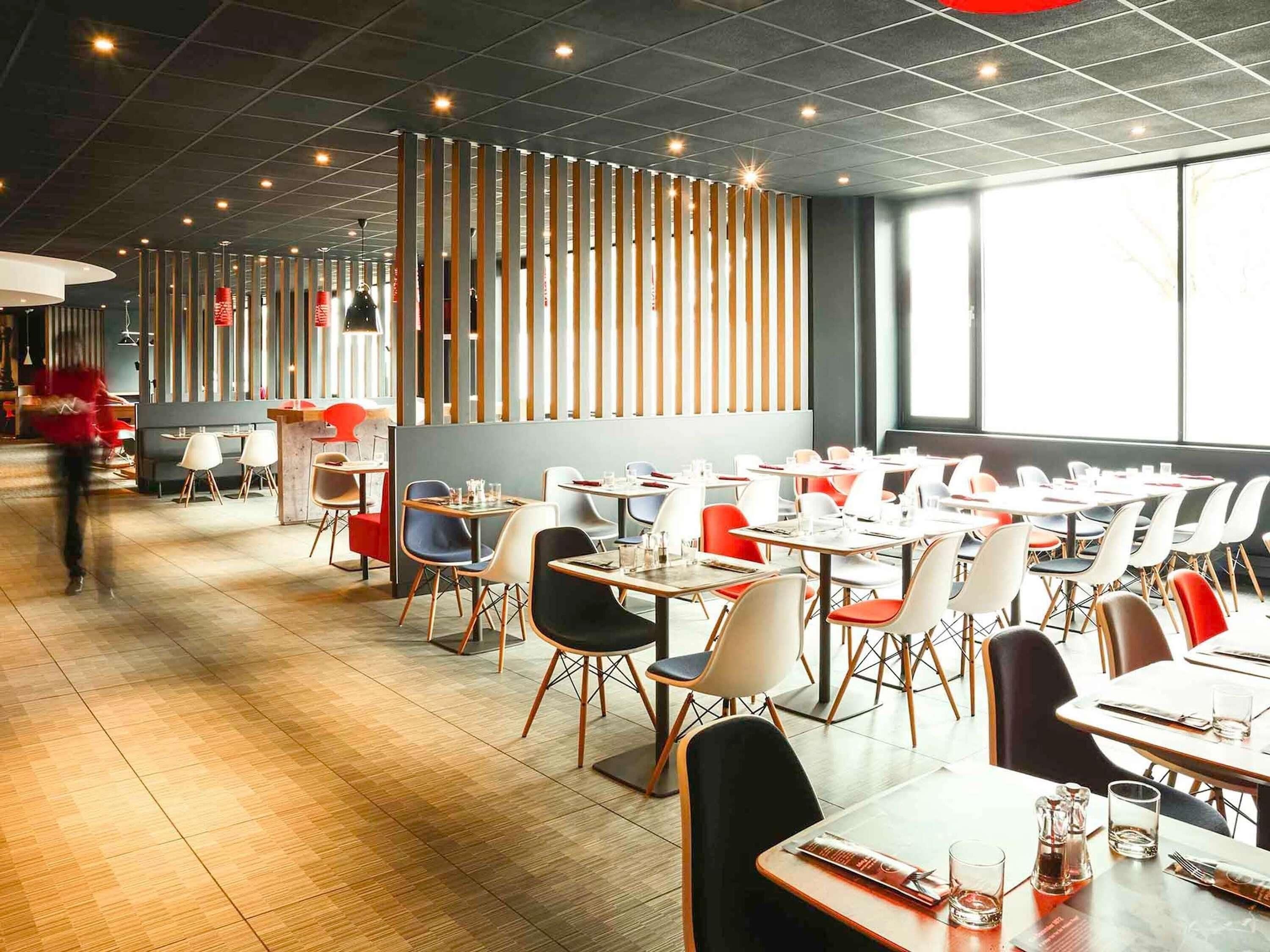 A modern restaurant with a long counter, multiple tables, and chairs.