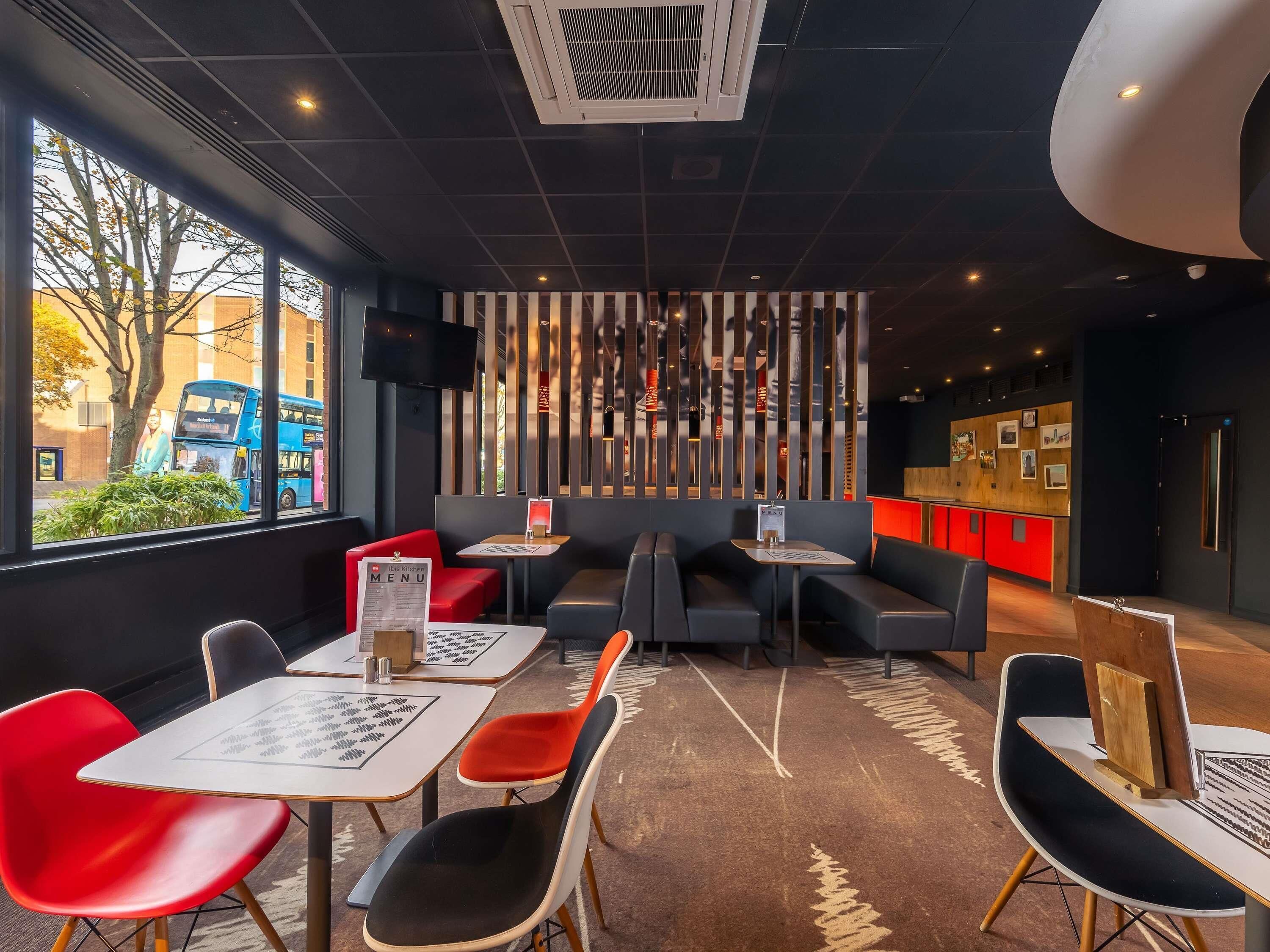 A modern restaurant interior with seating, a menu stand, and a view of the street outside.