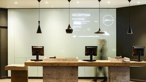 Un espace d’accueil doté d’un long comptoir de réception, de deux écrans et d’un écran de projection affichant les tarifs des chambres et les services proposés.