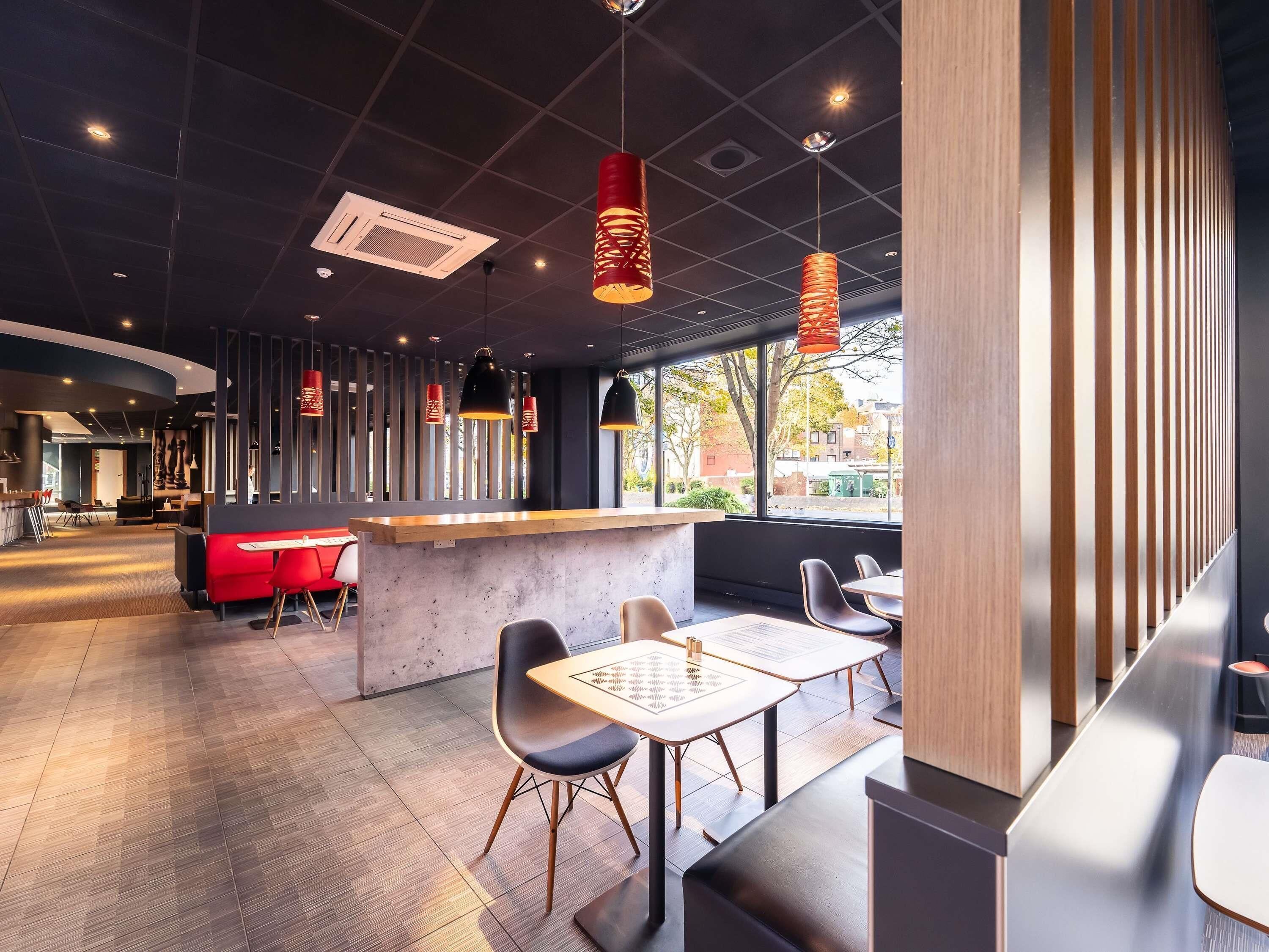 A modern restaurant interior with a bar area, seating, and a view through large windows.