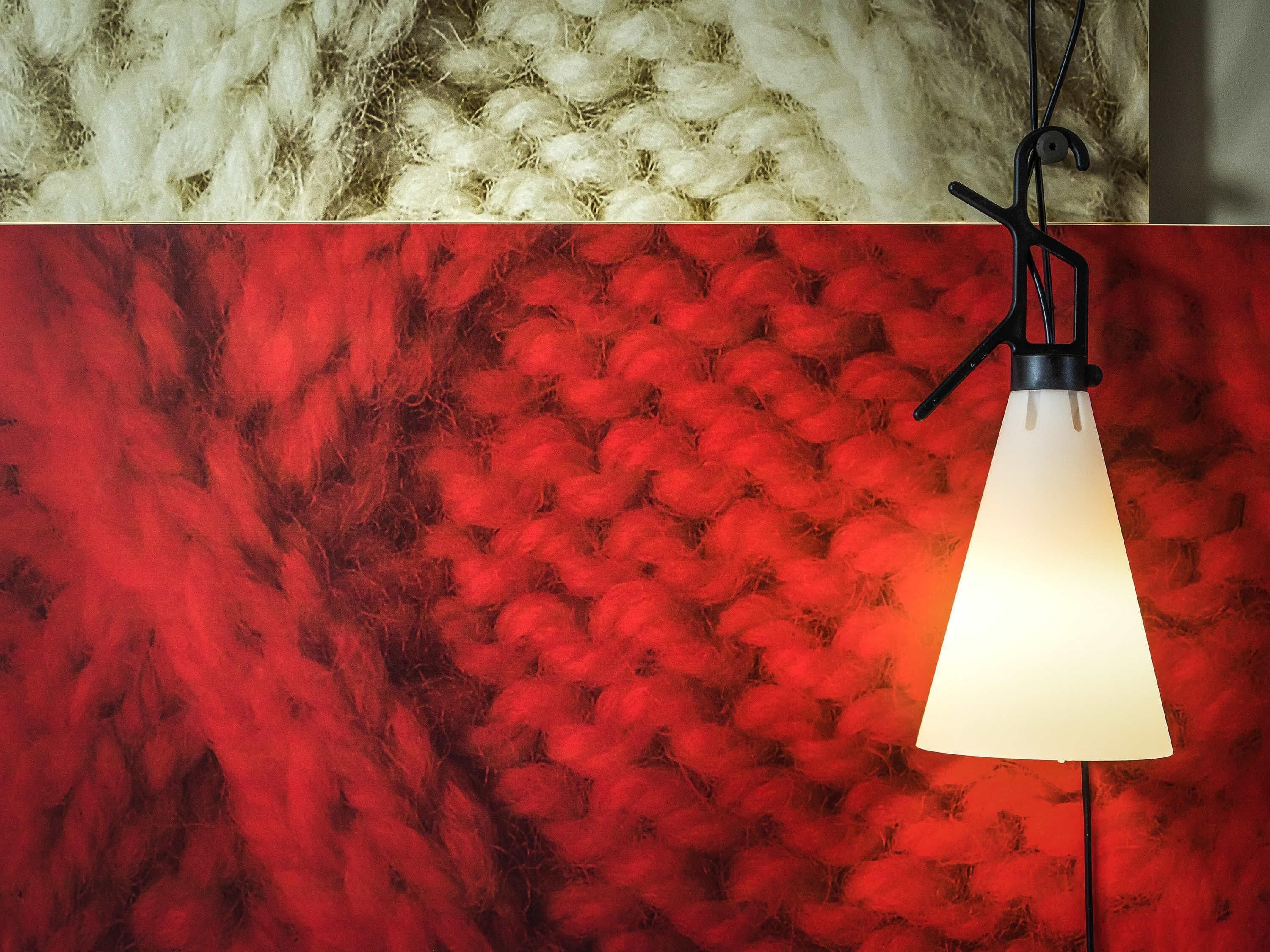A hanging light fixture with a white shade, a red textured wall, and a white fluffy area above.
