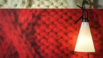 Una lámpara colgante con pantalla blanca, pared texturizada de color rojo y una zona mullida de color blanco arriba.