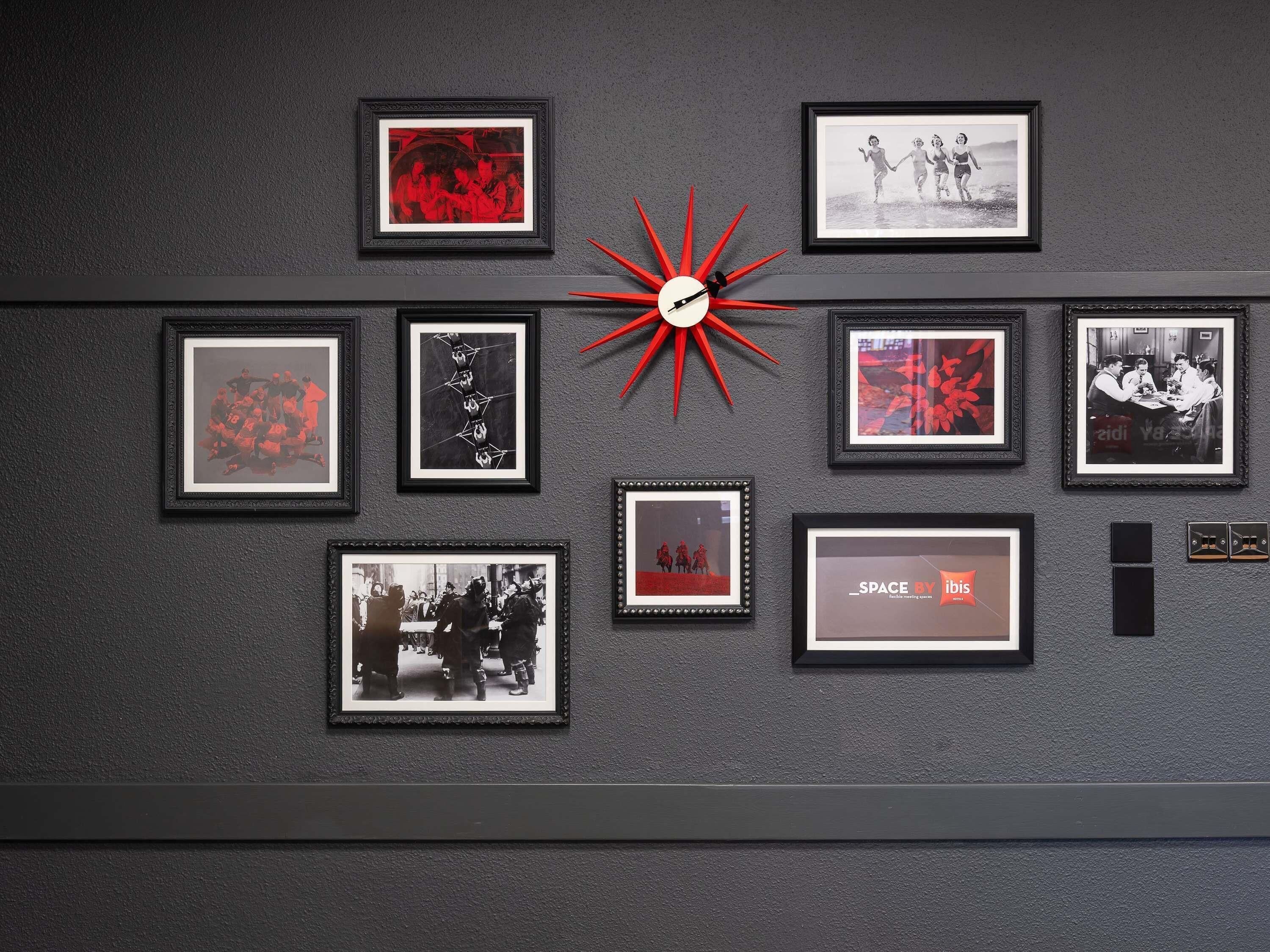 Un mur orné de plusieurs photographies encadrées et d’une horloge rouge en forme d’étoile.