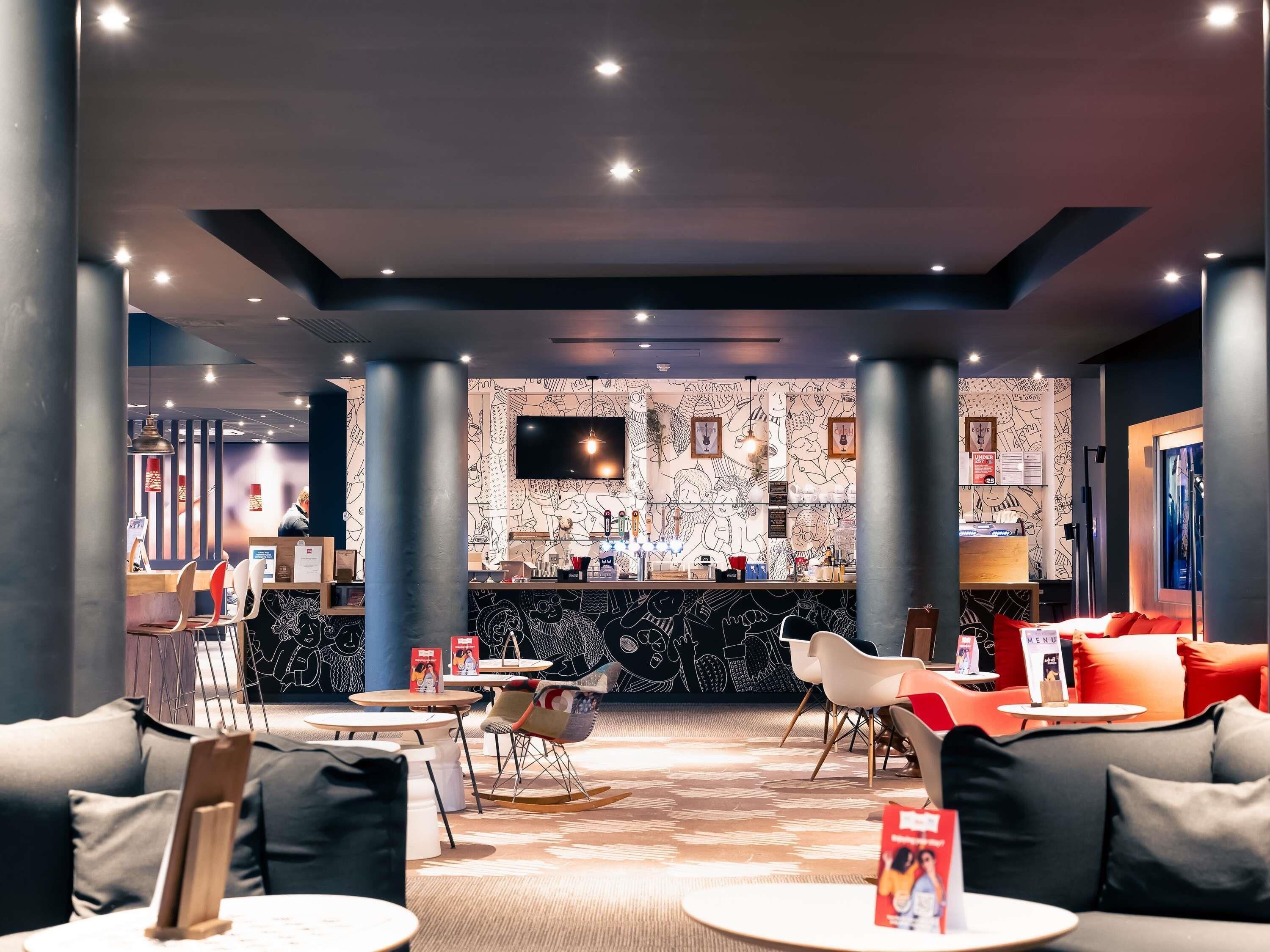 A modern lounge area with seating, a bar counter, and a large TV screen.