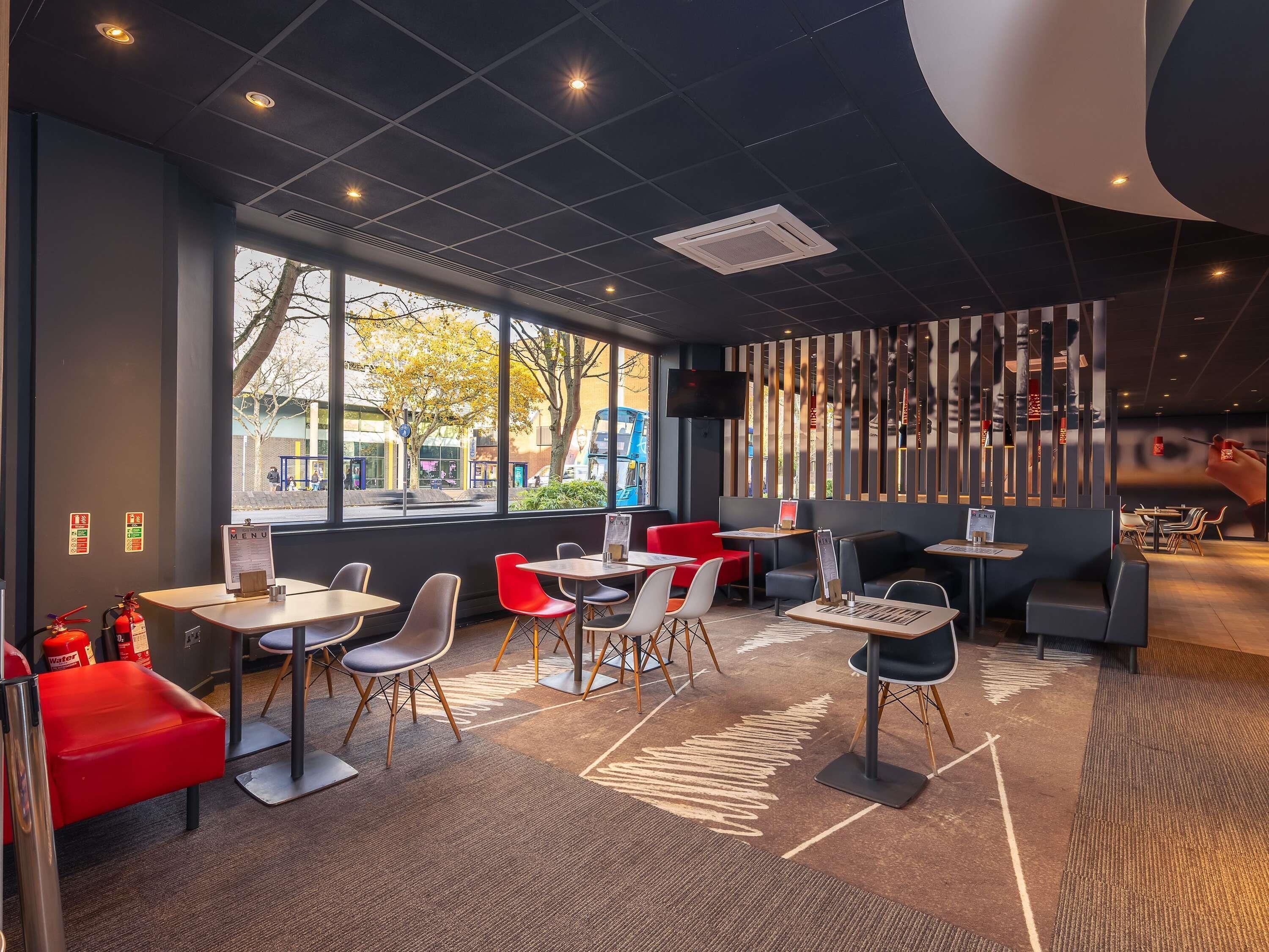 A modern restaurant interior with tables, chairs, and a large window offering an outdoor view.