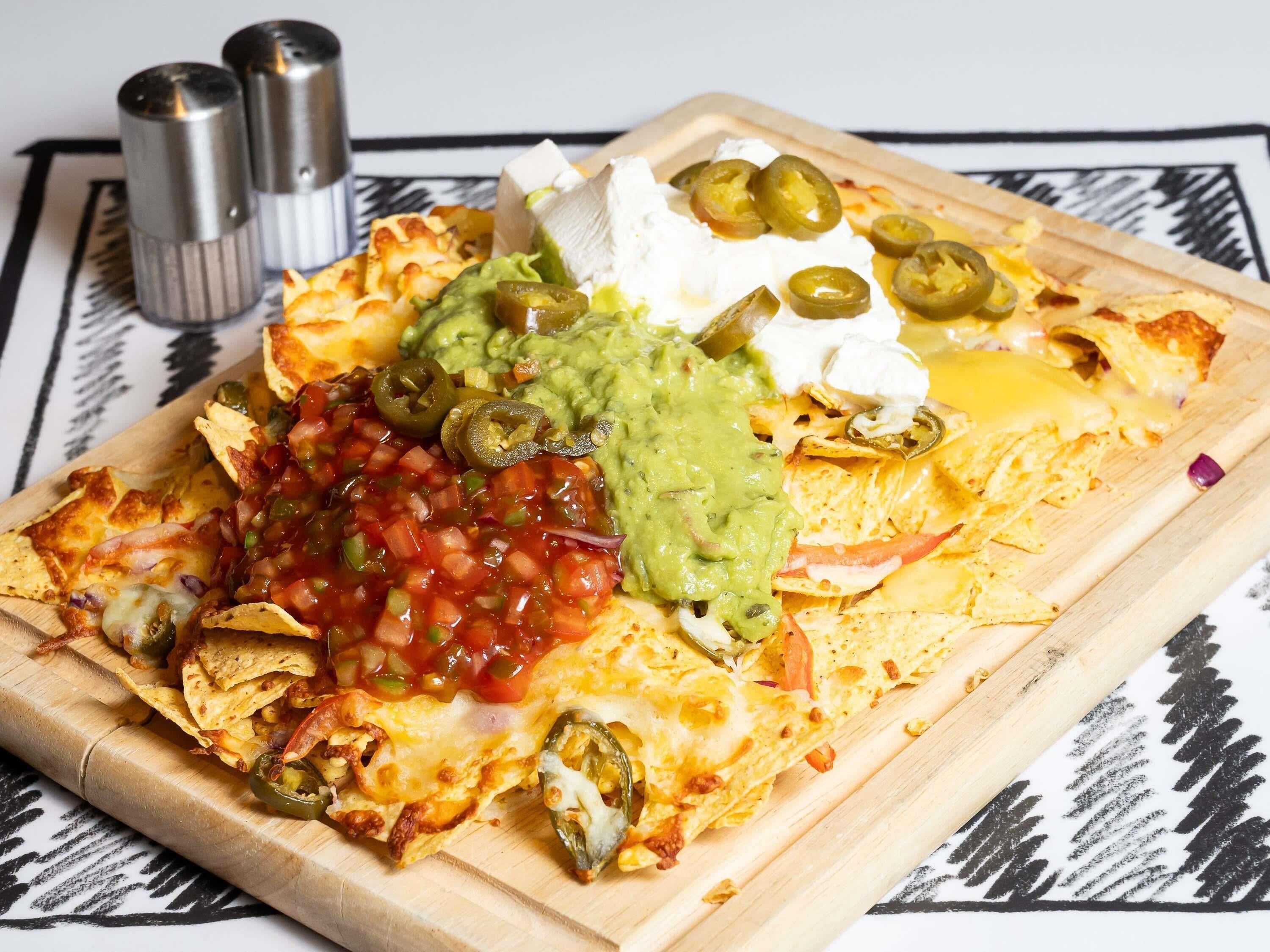 Nachos topped with cheese, guacamole, sour cream, and jalapeños on a wooden board.