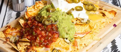 Nachos met kaas, guacamole, zure room en jalapeños op een houten plank.