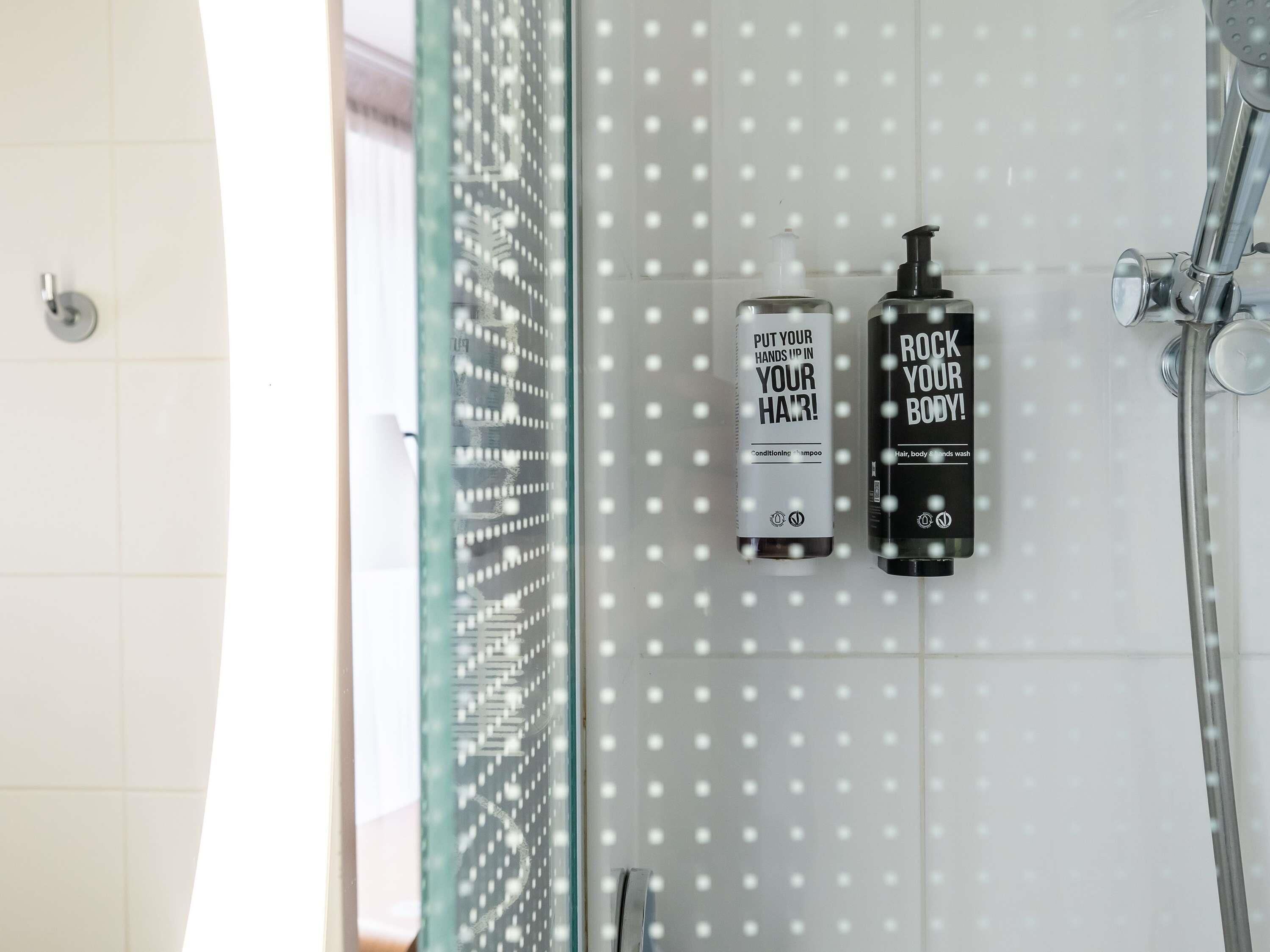 A bathroom with a glass shower door, two bottles of shampoo, and a handheld showerhead.