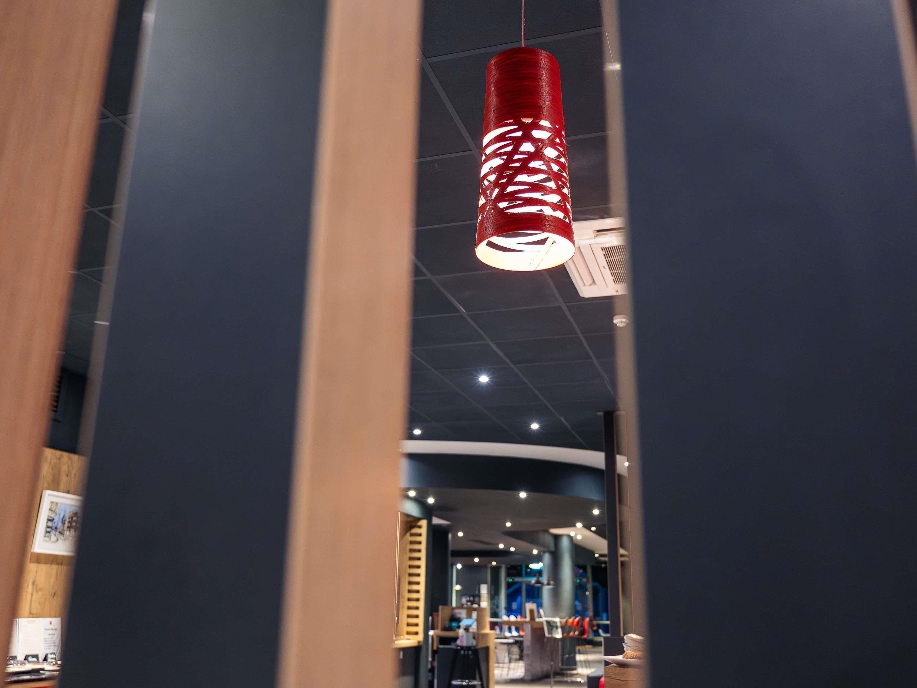 A modern interior with a hanging red cylindrical light fixture, a wooden door frame, and a curved ceiling with recessed lighting.