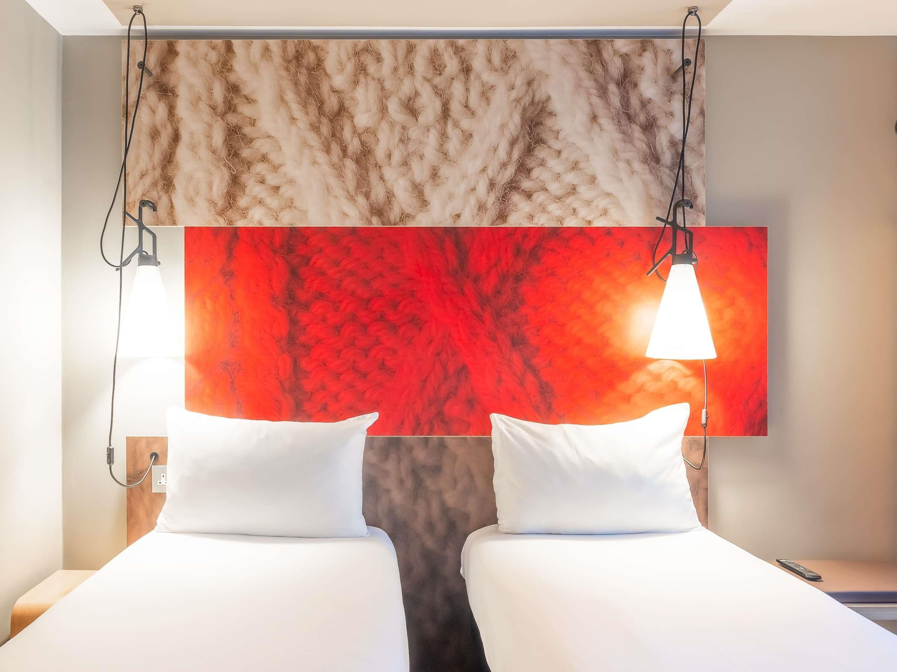 Une chambre d’hôtel avec deux lits, un grand tableau abstrait rouge et un mur à la texture évoquant le marbre.