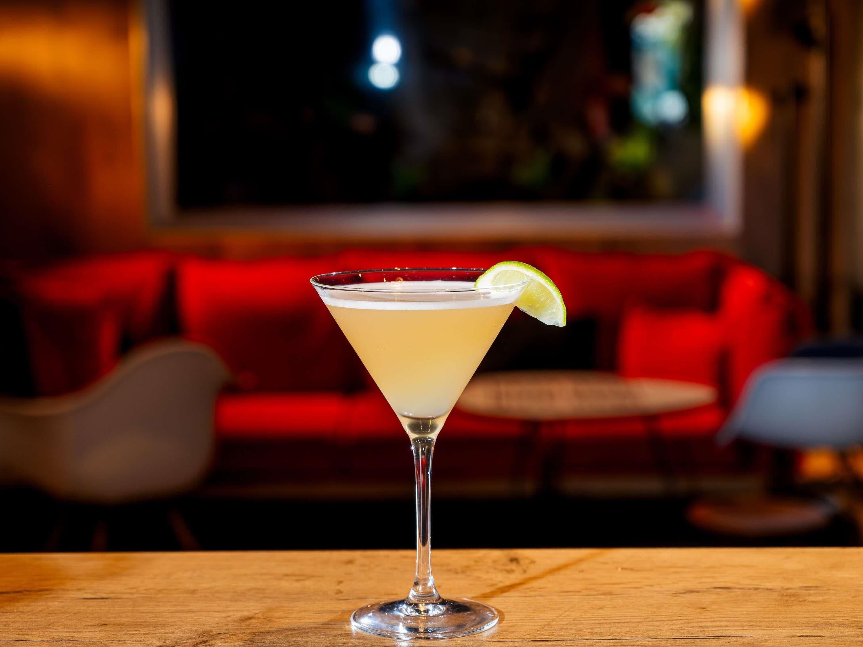 Ein Cocktail im Martiniglas mit Limettenscheibe auf einem Holztisch.