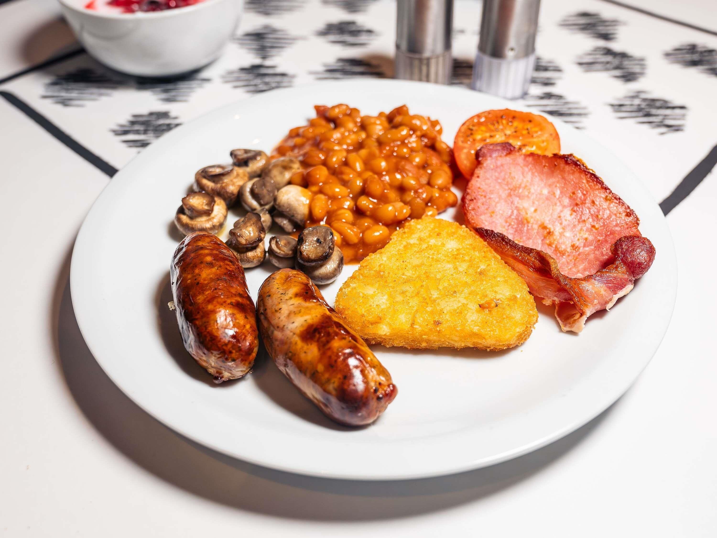 A plate of food with sausages, mushrooms, baked beans, a slice of ham, and a piece of cornbread.