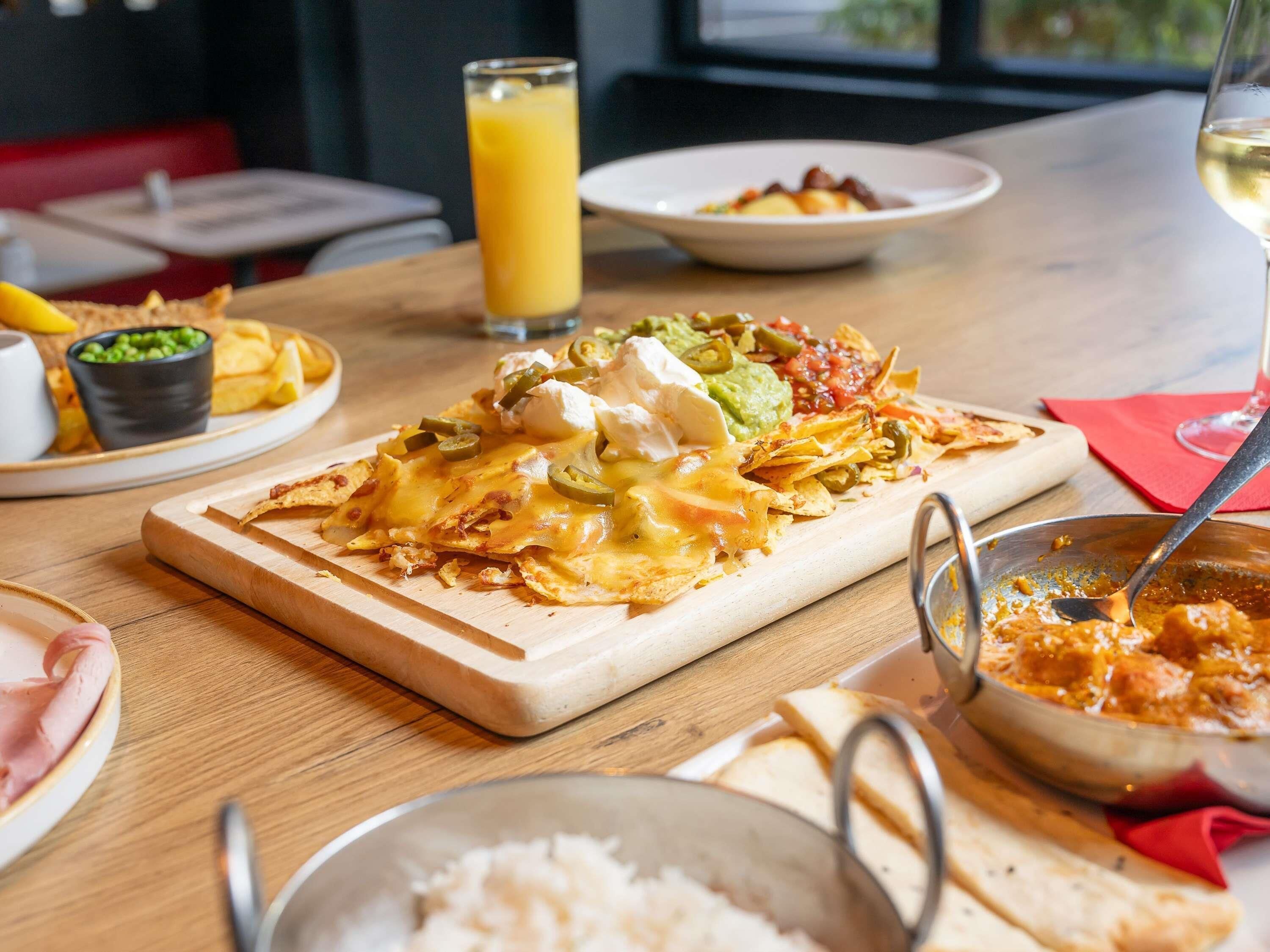 A meal with nachos topped with cheese, jalapeños, and sour cream, accompanied by a glass of orange juice and a bowl of salsa.