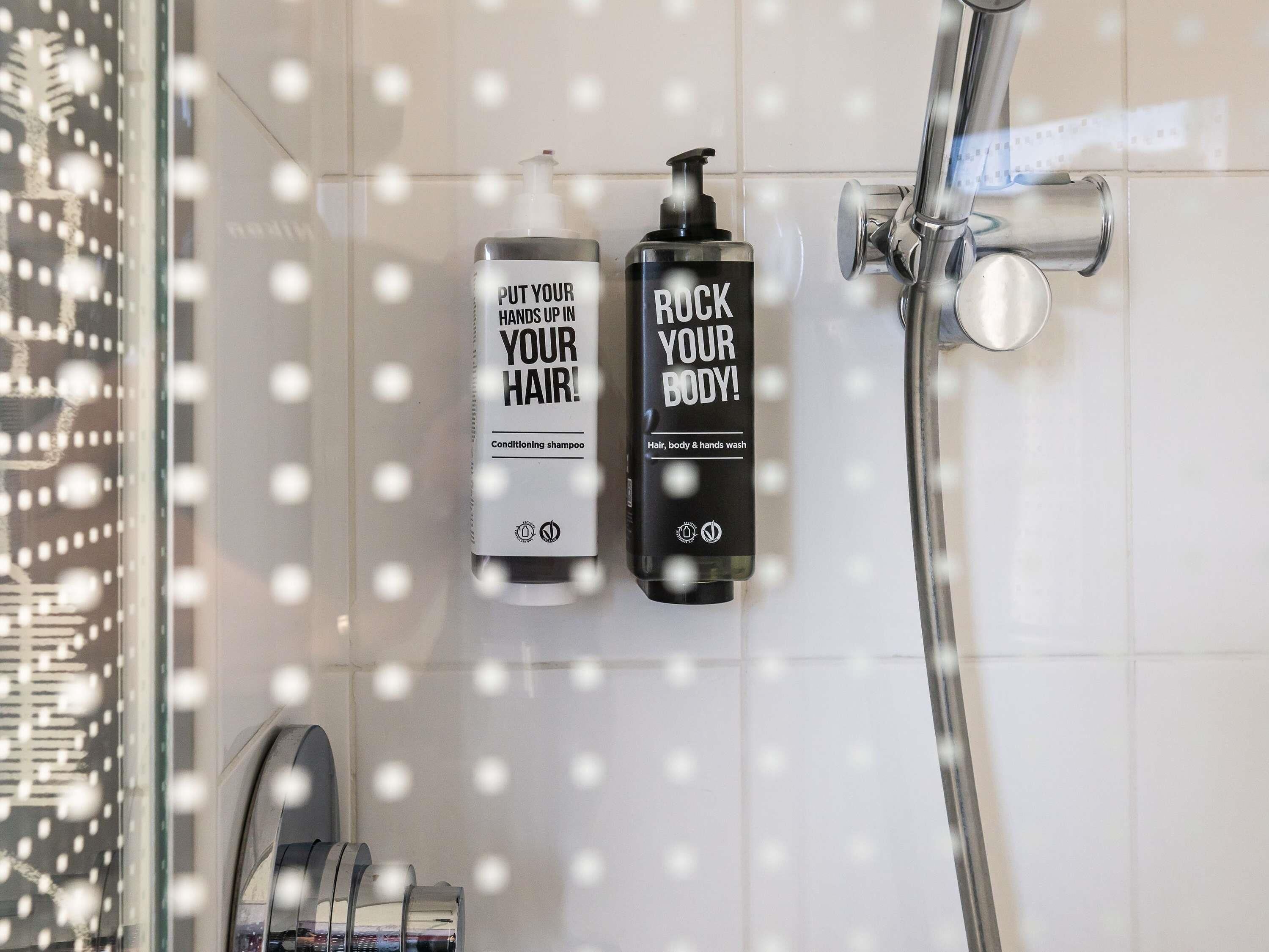Two bottles of hair and body wash in a shower area with a glass door.
