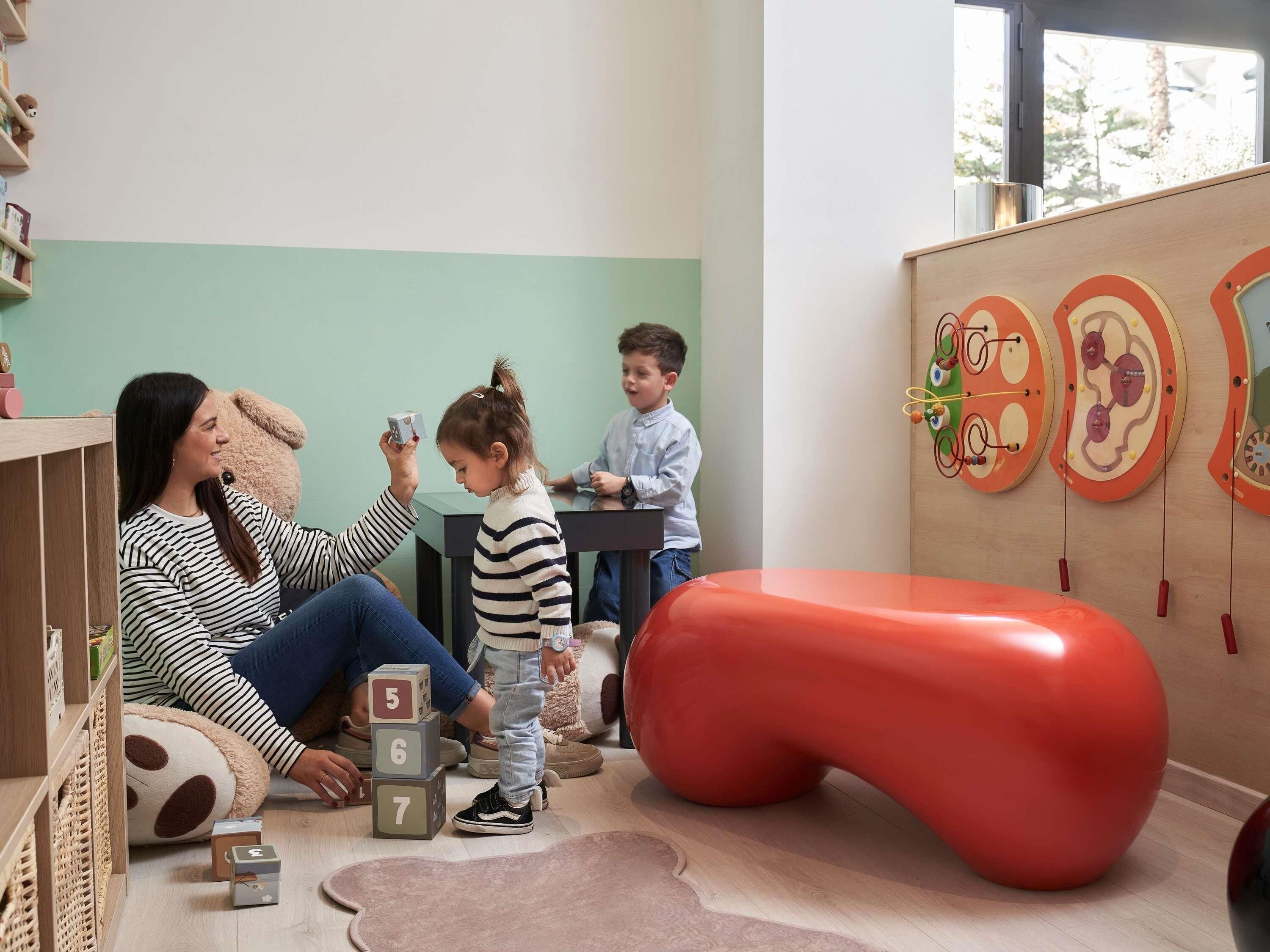 Une pièce avec un plancher en bois, un pouf rouge en forme de haricot et un enfant qui joue avec des blocs de construction.
