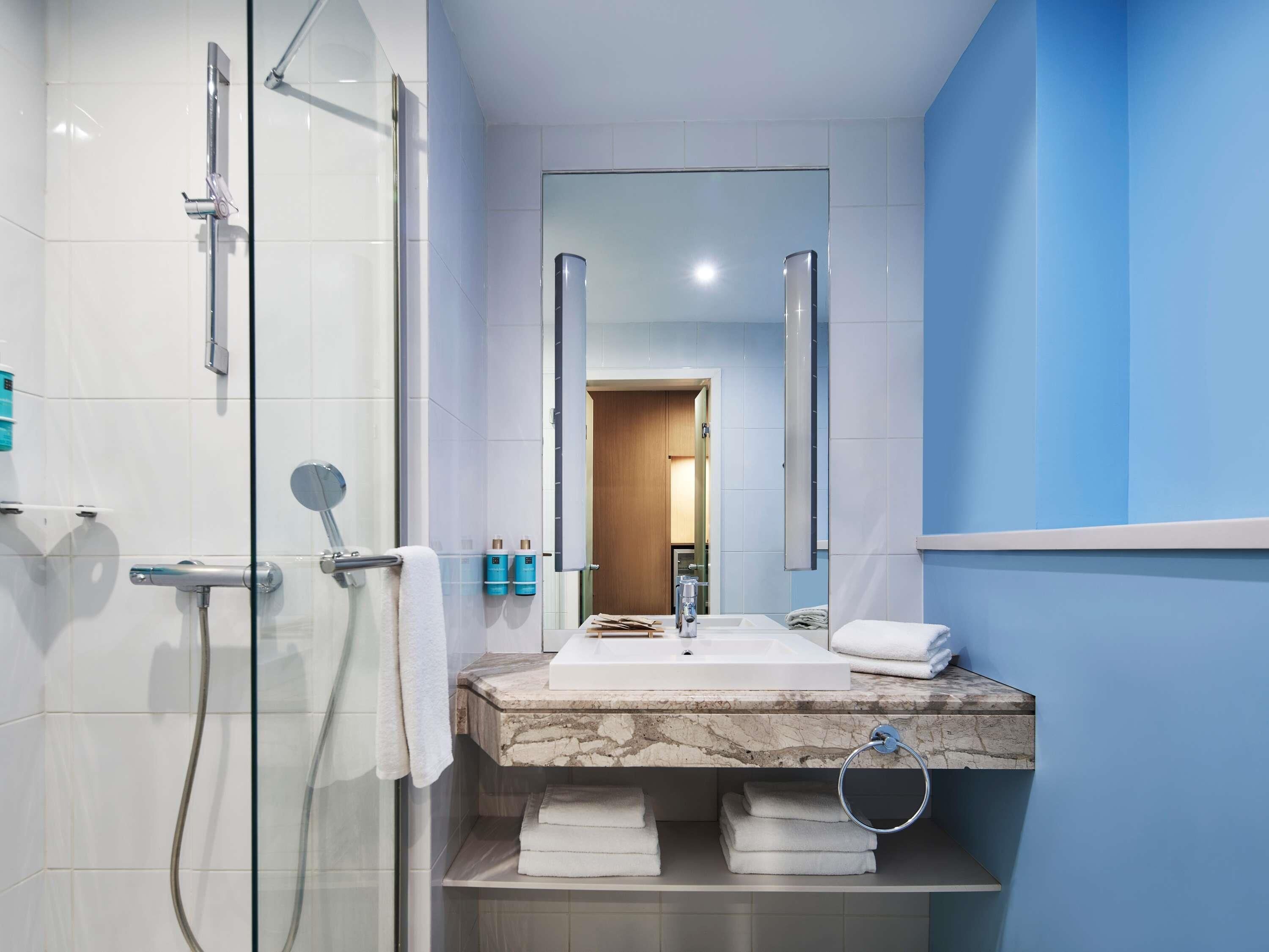 A modern bathroom with a glass shower enclosure, a marble sink, and a large mirror.