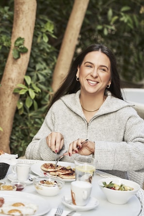 A person dining at an outdoor table with various dishes, a cup, and a glass.