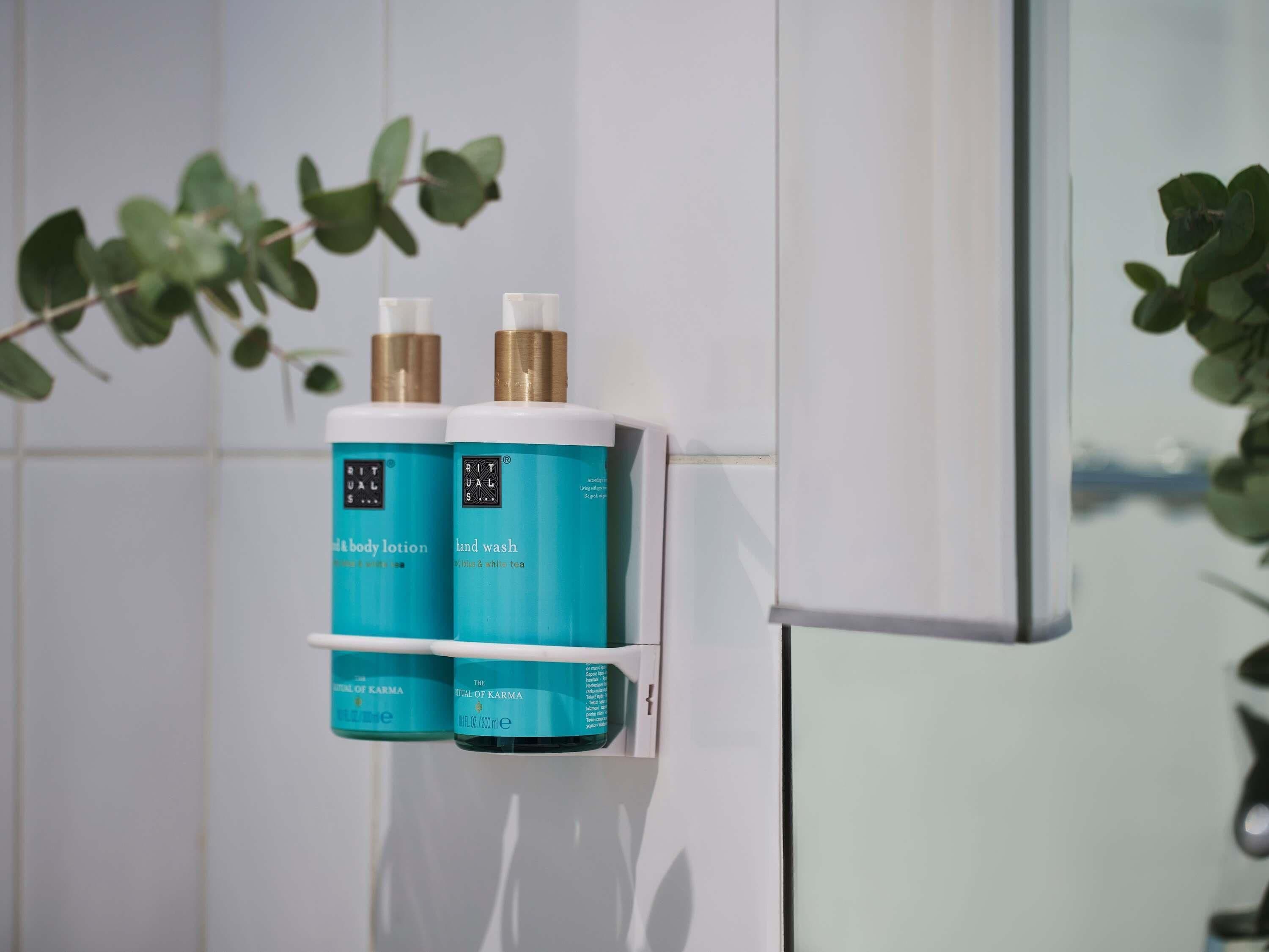 Une salle de bain avec un mur blanc et une étagère sur laquelle sont posés deux flacons de savon pour les mains et de lotion pour le corps.