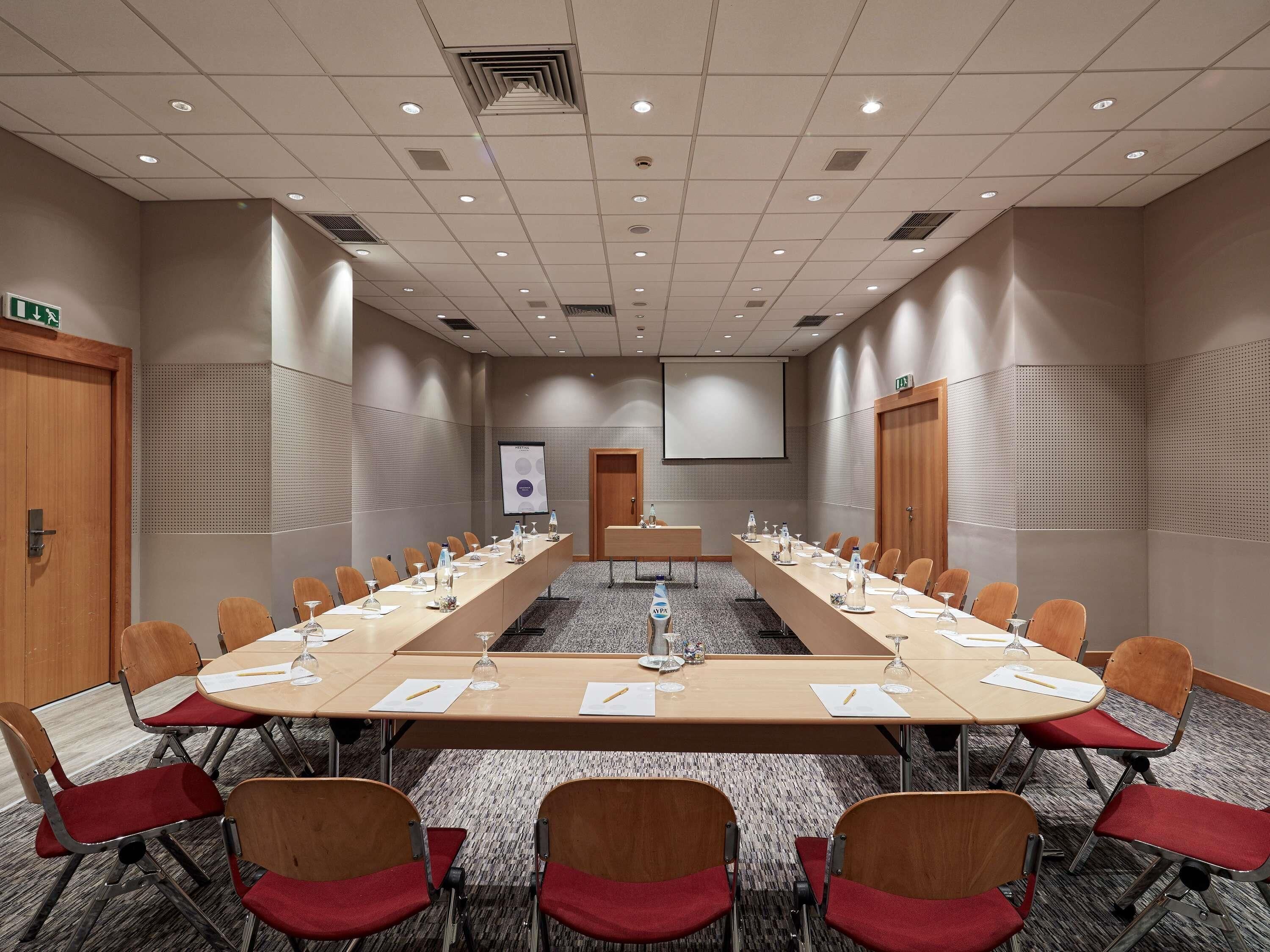 A conference room with a long table, chairs, a projector screen, and a carpeted floor.