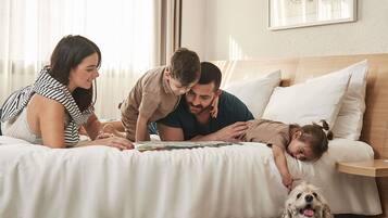 A family on a bed with a dog, in a room with a wooden headboard and a framed picture on the wall.