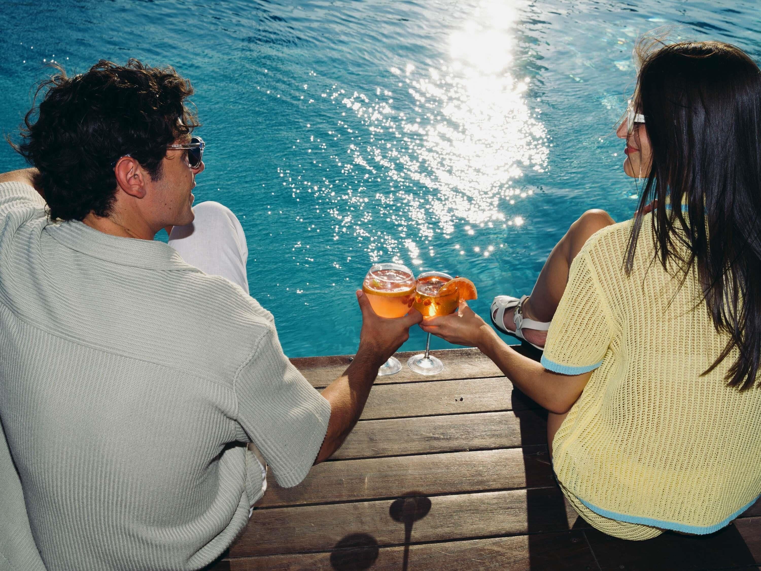 Two people toasting with drinks by a poolside.