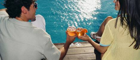 Two people toasting with drinks by a poolside.