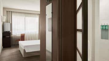 Une chambre d’hôtel équipée d’un lit, d’un bureau, d’une chaise, d’une télévision et d’une salle de bain avec un porte-serviettes.