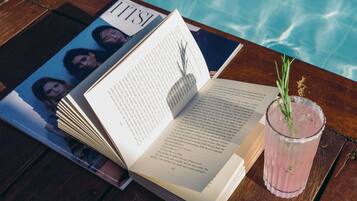 A book, a magazine, and a drink on a wooden table by a pool.