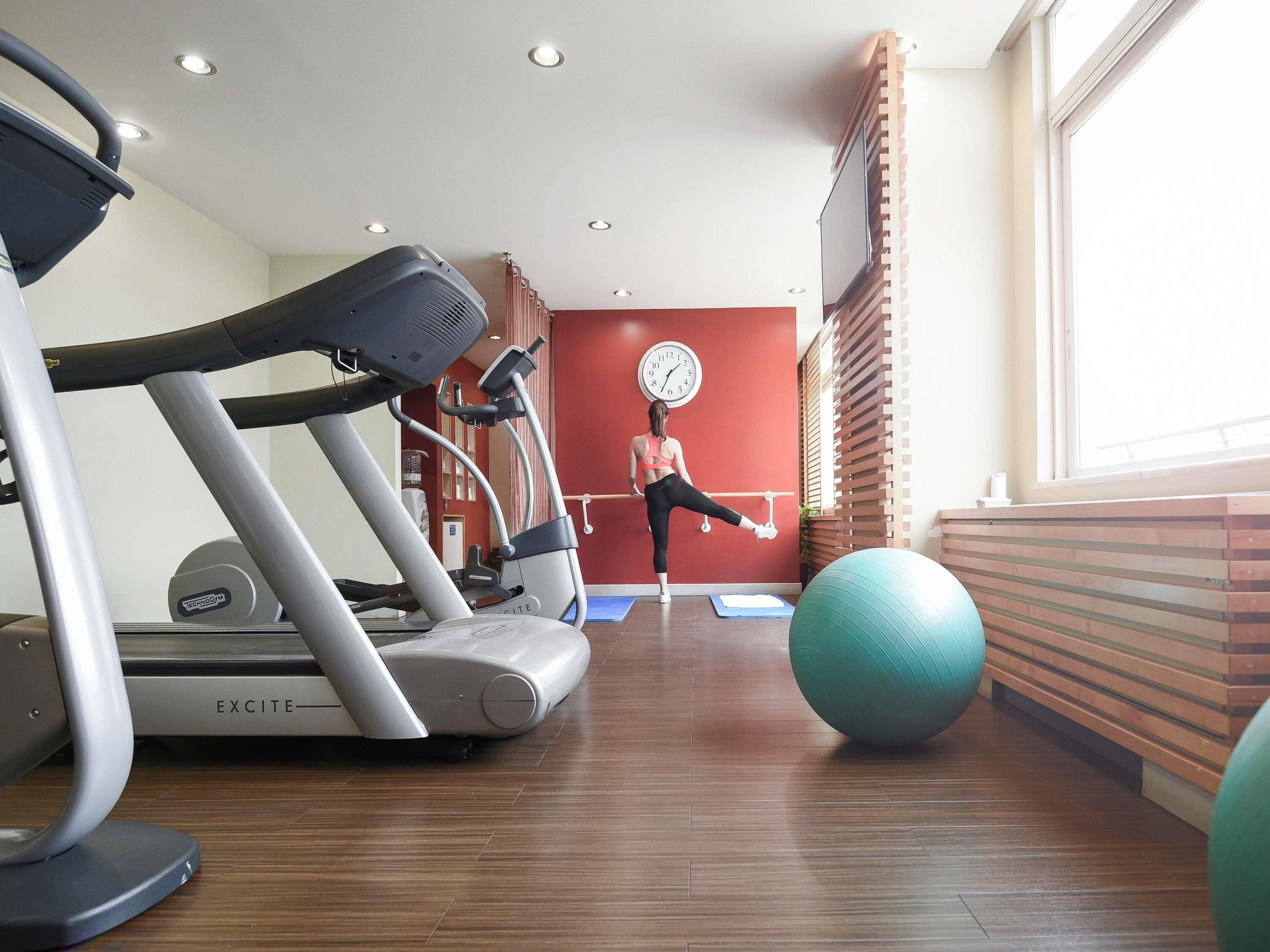 Une salle de sport équipée de tapis de course, d’une horloge murale et de ballons d’exercice.