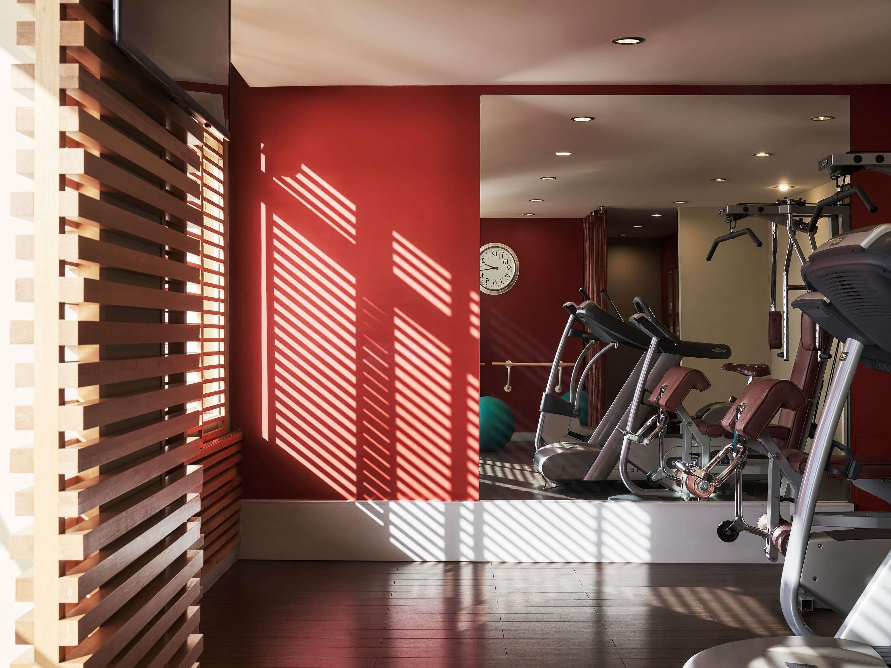 A gym with exercise equipment, a clock on the wall, and a wooden slatted wall design.