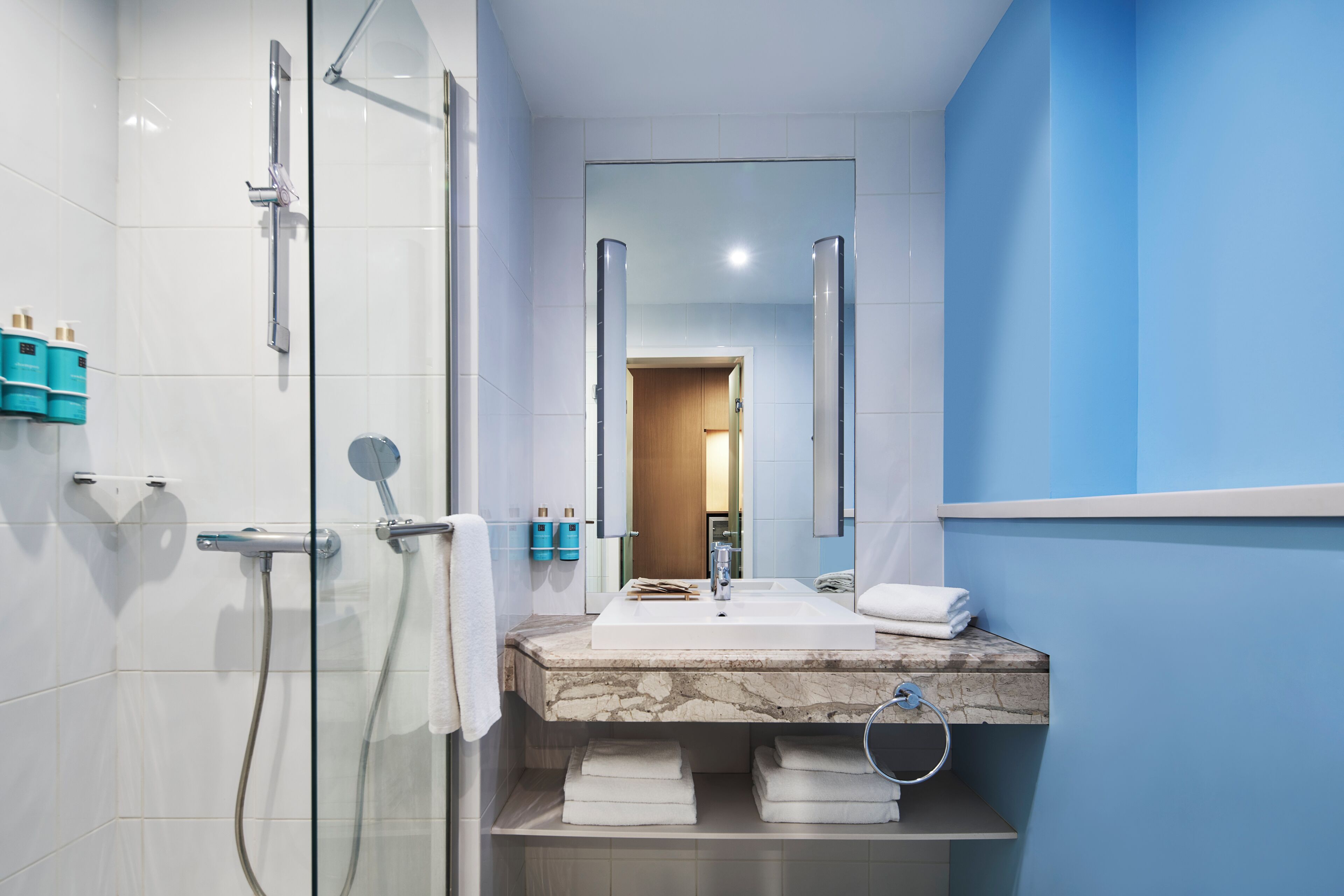 A modern bathroom with a glass-enclosed shower, a marble sink, and a mirror above it.