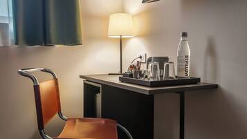 Habitación de hotel con escritorio, silla, lámpara, botella y cafetera.