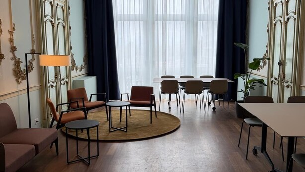 A room with a wooden floor, a sofa, a table with chairs, a lamp, and a large window with curtains. - BYPILLOW Grand Central (Padova)