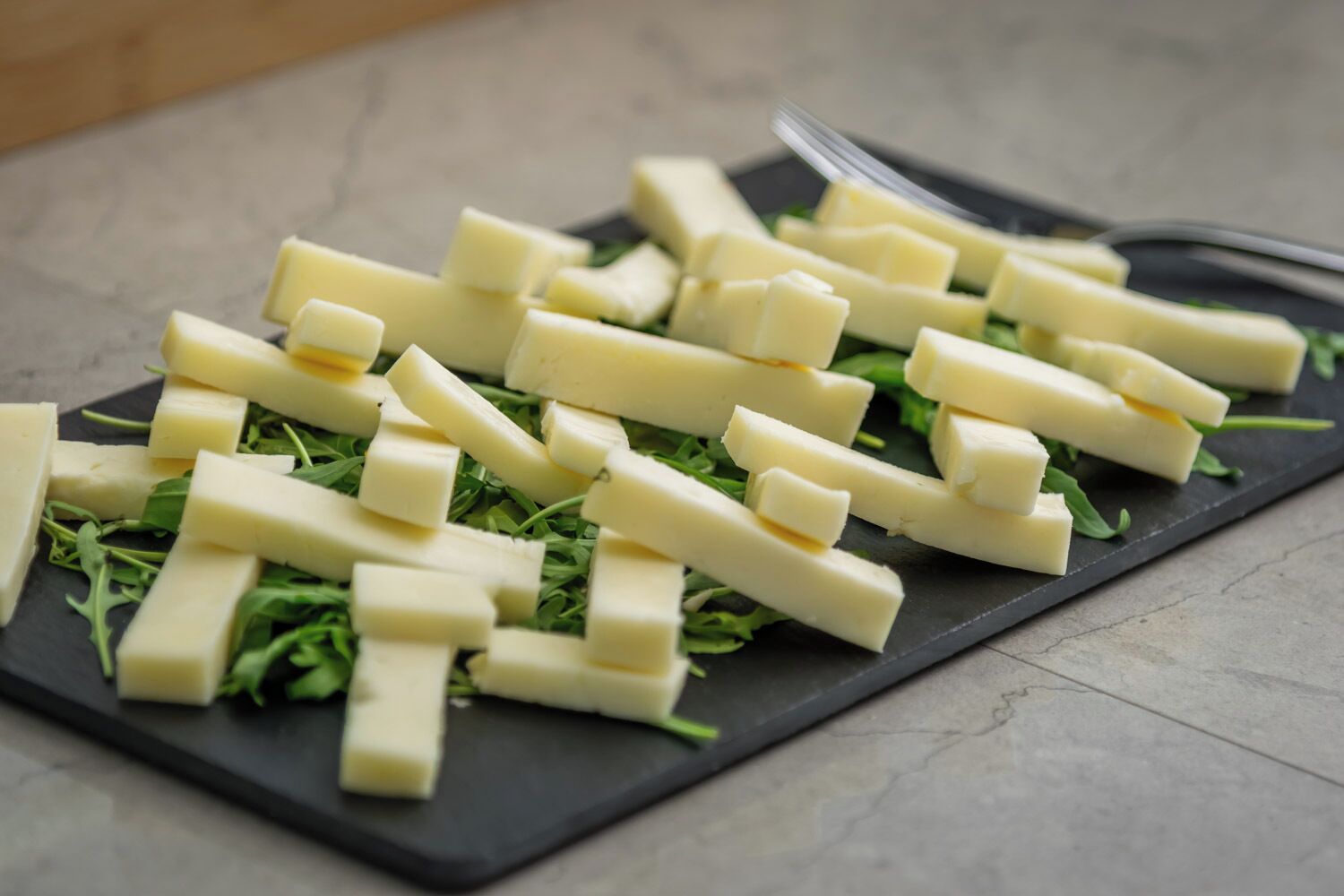A black slate board with cheese and greens.