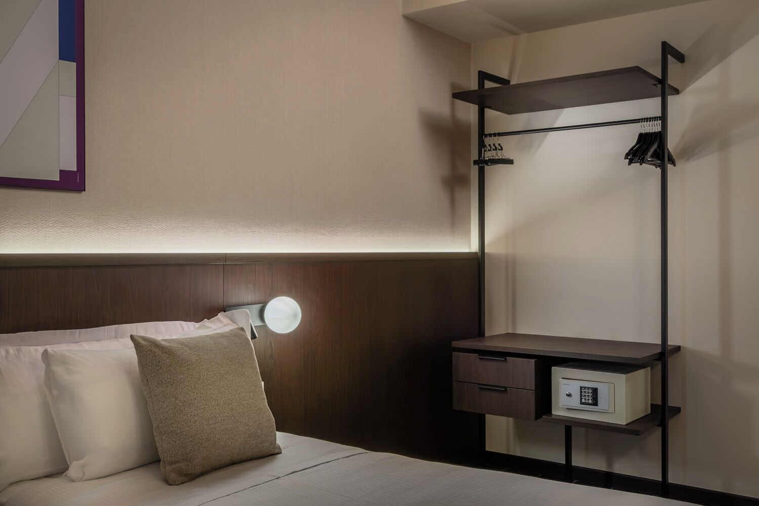 Ein Hotelzimmer mit Bett, Nachttischlampe, Schreibtisch mit Stuhl und Kleiderschrank.