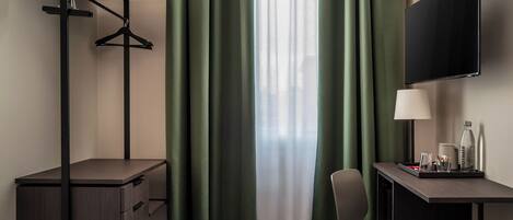 Una habitación de hotel con escritorio, silla, televisor y ventana con cortinas verdes.