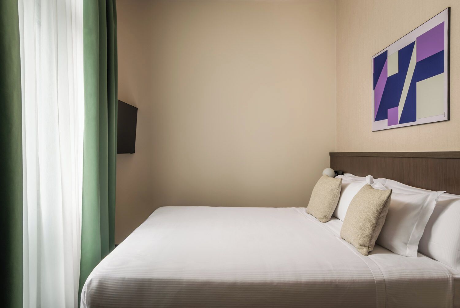 Una habitación de hotel con una cama, un televisor de pared y un cuadro.