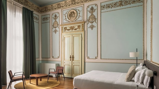 A room with a bed, two chairs, a round table, a lamp, and a wardrobe. - BYPILLOW Grand Central (Padova)