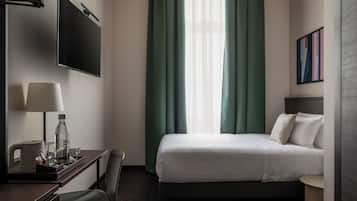 Ein Hotelzimmer mit Bett, Schreibtisch mit Lampe, Fernseher und einem Fenster mit Vorhängen.