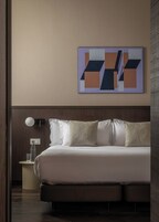 Una habitación de hotel moderna con una cama grande, una mesita de noche con lámpara y una obra de arte abstracta en la pared.