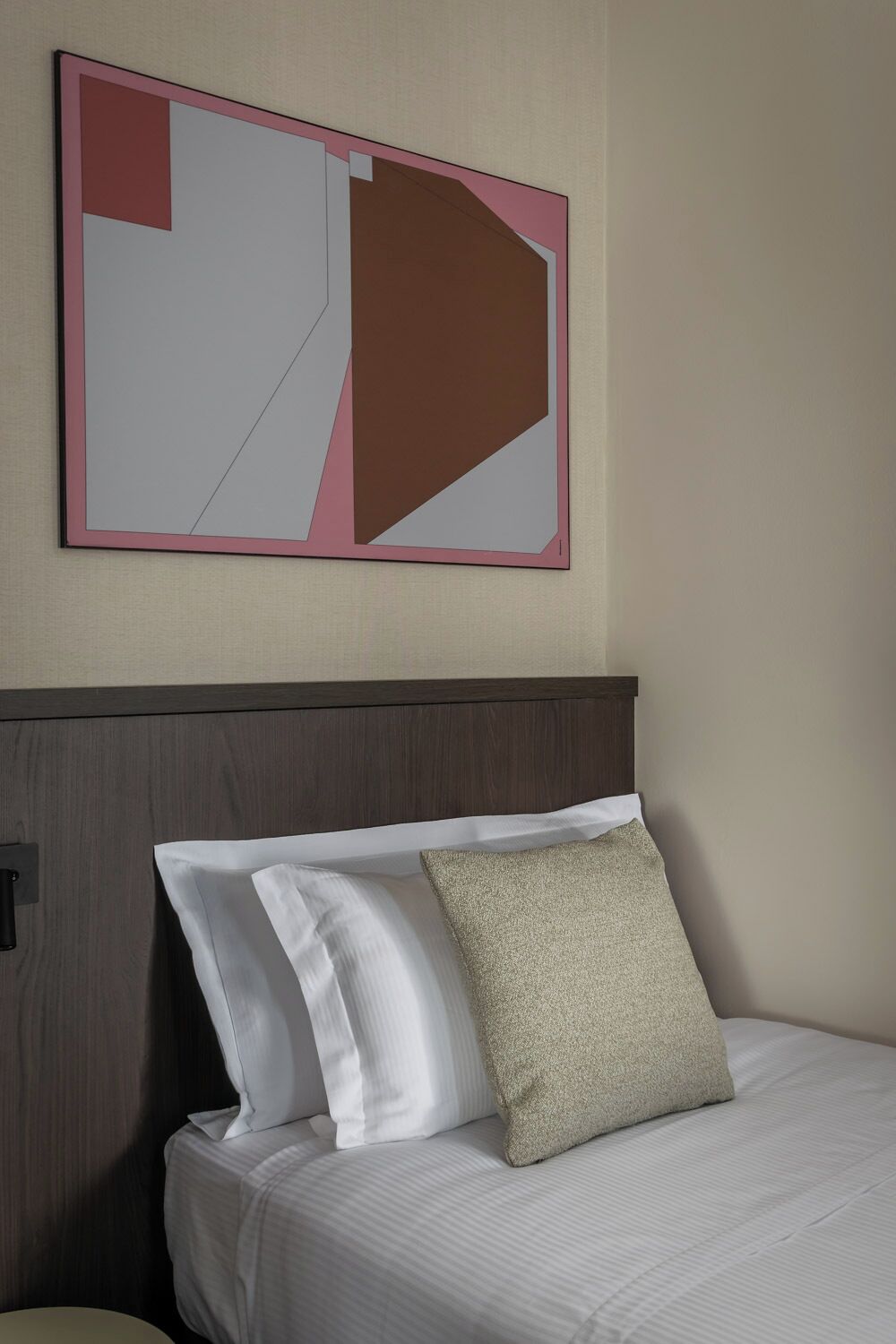 A hotel room with a bed, pillows, a headboard, and a wall-mounted artwork.