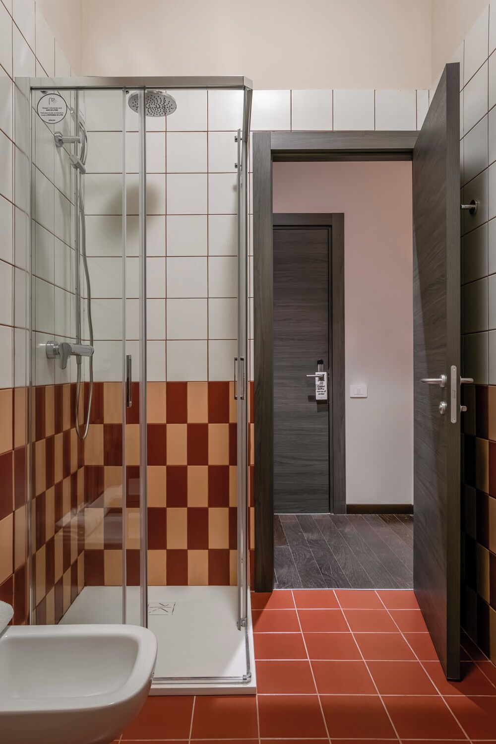 Un bagno con doccia, un water e una porta che dà su un'altra stanza.