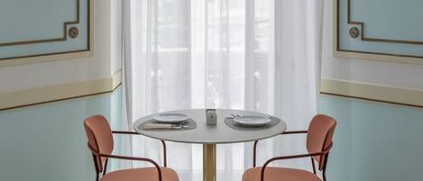 Una habitación con una mesa redonda, dos sillas, un ventanal con cortinas translúcidas y lámparas de pared.